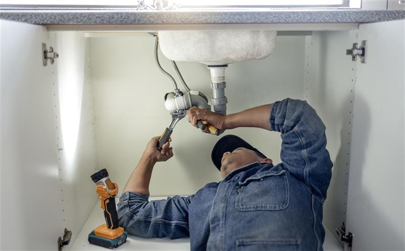 Plumber repairing pipes beneath a bathroom sink in Corvallis