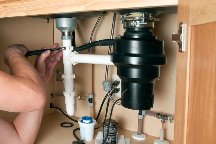 Plumber installing a garbage disposal beneath a kitchen sink in Corvallis