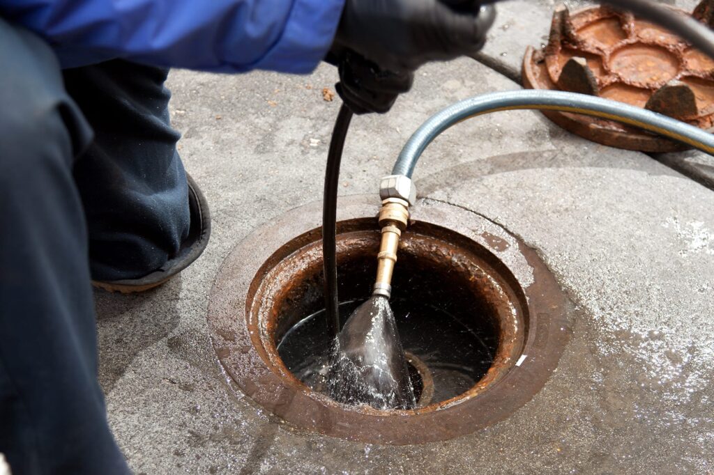 Plumber hydro jetting a sewer line through a manhole in Corvallis