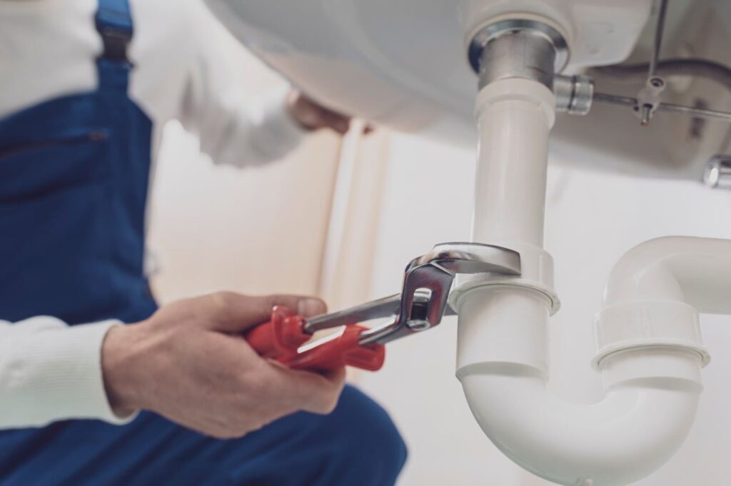 Plumber repairing a white drain pipe beneath a sink in Corvallis