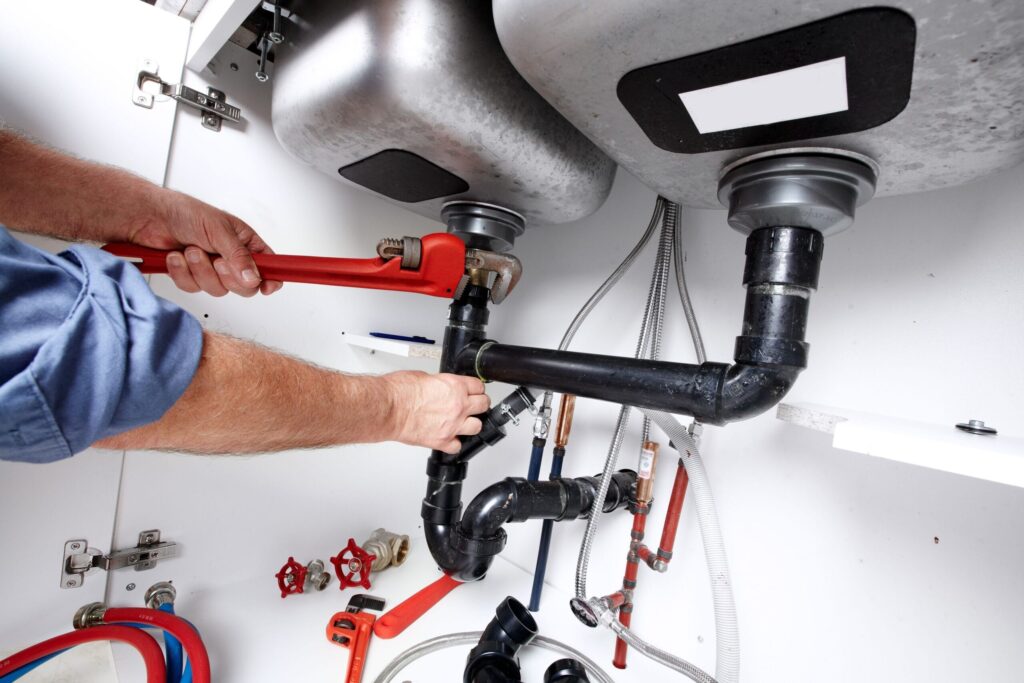 Plumber repairing drain pipes beneath a kitchen sink in Corvallis
